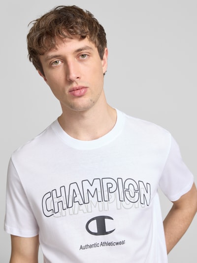 Männermodel trägt T-Shirt mit Label-Print und Rundhalsausschnitt von CHAMPION, weiße Baumwolle, Regular Fit, Nahaufnahme Oberkörper.