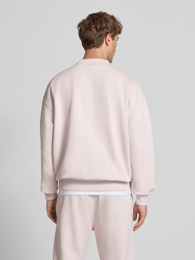Männermodel trägt Oversized Sweatshirt mit Label-Stitching von Pegador aus Baumwoll-Mix in hellem Rosa, Rückenlänge 70 cm, ganzkörperansicht Rückansicht.