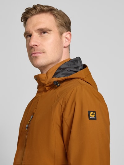 Männermodel trägt Jacke mit Napoleontasche Modell 'KOS' von Killtec in Orange mit Kapuze, Ärmelriegel, Label-Patch, Nahaufnahme Oberkörper.