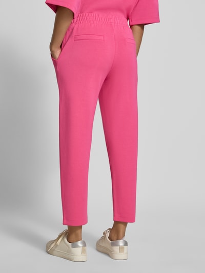 Frauenmodel trägt Sweatpants mit seitlichen Eingrifftaschen von Christian Berg Woman in Pink, lockere Passform, Ganzkörperansicht Rückansicht.