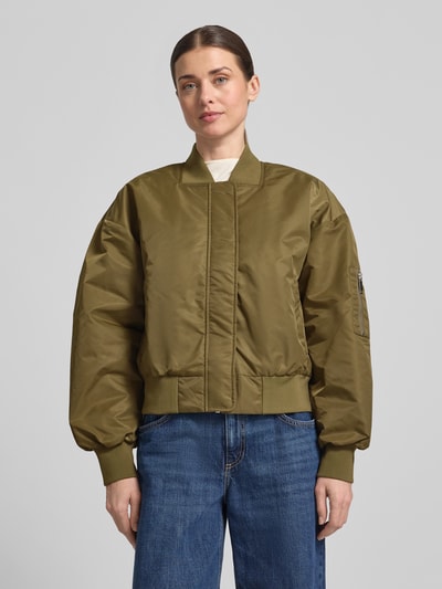 Vrouwenmodel draagt olijfgroene Regular Fit Bomberjacke mit Stehkragen Modell 'Helga' van My Essential Wardrobe met elastische boorden, steekzakken en mouwzak met ritssluiting, textuur glad, voorkant volledig zichtbaar, bovenlichaam close-up.