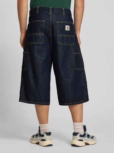 Männermodel trägt Jeans-Bermudas aus reiner Baumwolle Modell 'Double' von Carhartt Work In Progress, dunkles Blau, Kontrastnähte, Loose Fit, 5-Pocket-Design, Ganzkörperansicht Rückansicht, Kontext: Herren Jeans-Bermudas, Knopf- und Reißverschluss, Gürtelschlaufen, Bundweite Größe M 44 cm, Innenbeinlänge 41 cm.