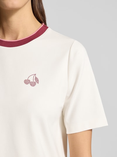Frauenmodel trägt Regular Fit T-Shirt mit Strasssteinbesatz von Marc Cain in Offwhite mit Rundhalsausschnitt und elastischem Baumwoll-Mix, Nahaufnahme Oberkörper.