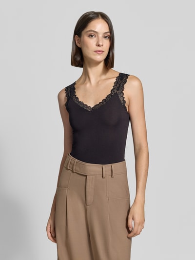 Frauenmodel trägt Slim Fit Tanktop aus Viskose-Mix Modell 'ROSA' von VERO MODA in Schwarz, glatte Textur, beige Hose, Ganzkörperansicht von vorne.