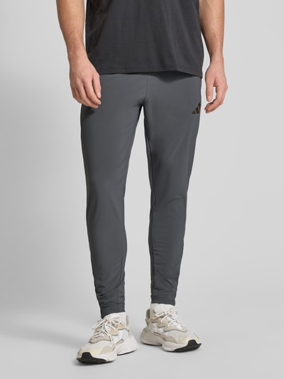 Männermodel trägt Regular Fit Jogpants mit elastischem Bund Modell 'TIRO' von adidas Sportswear in Dunkelgrau, Nahaufnahme Unterkörper. Elastischer Material-Mix, Reißverschluss am Beinabschluss, Kordelzug und Seitentaschen sichtbar, Innenbeinlänge 71 cm bei Größe M.
