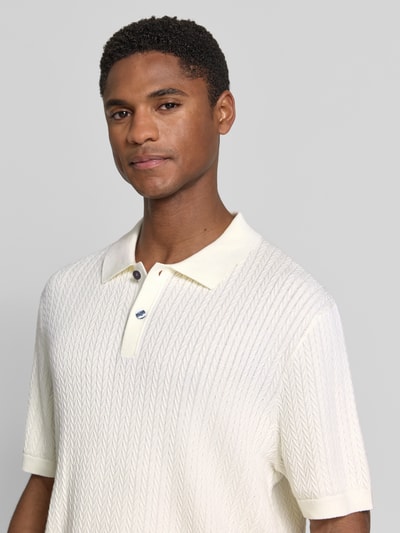 Mężczyznamodel nosi koszulkę polo Regular Fit Poloshirt mit Strukturmuster von Christian Berg Men, jasny fakturowany wzór, kołnierzyk polo, krótka listwa guzikowa, długość tyłu 72 cm w rozmiarze M, długość rękawów 25 cm w rozmiarze M, zbliżenie na górną część ciała.