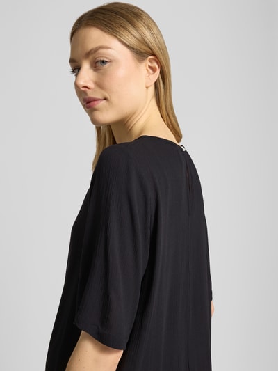 Vrouwenmodel draagt Relaxed Fit T-shirt uit zuiver viscose model 'Marrakech' van ICHI, dames t-shirt met ronde hals, ruglengte bij maat S 58 cm, mouwlengte bij maat S 29 cm, textuur met fijne plooien, effen zwart, detailopname bovenlichaam schuin achteraan.
