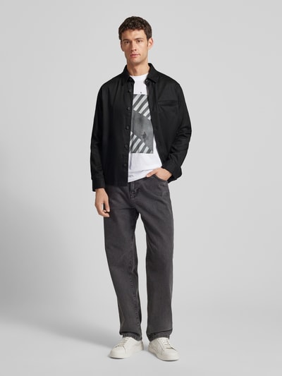 Männermodel trägt Regular Fit Hemdjacke aus Lyocell-Baumwoll-Mix Modell 'ENOCK' von HUGO in Schwarz mit Knopfleiste und Brusttasche, Ganzkörperansicht von vorne.