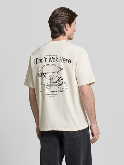Mężczyzna nosi T-Shirt mit Label-Print Modell 'Baine' von WOODBIRD w kolorze kremowym, czarny nadruk na plecach, czysta bawełna, krój regular fit, widok całej sylwetki z tyłu.