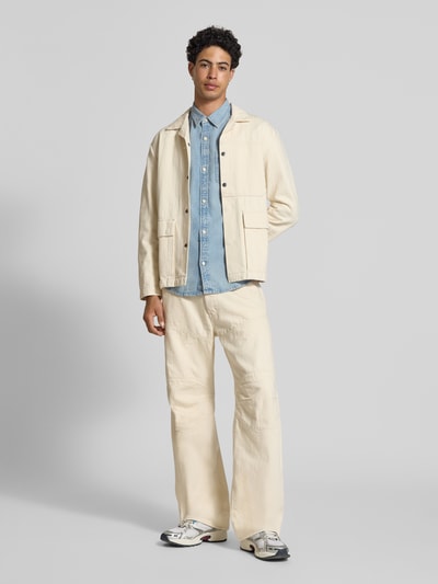 Männermodel trägt Regular Fit Jeanshemd aus reine Baumwolle van Calvin Klein Jeans in denimlook met borstzak, labelpatch en kentkraag, ganzkörperansicht von vorne.