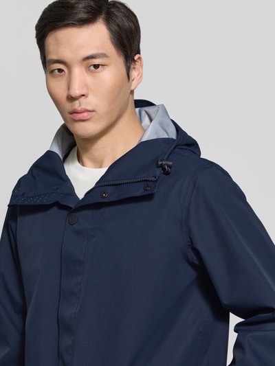 Männermodel trägt dunkelblaue Regenjacke mit Kapuze, Kordelzug, Reißverschlusstaschen, Modell 'RAIN EATER' von GOFRANCK, Nahaufnahme Oberkörper.