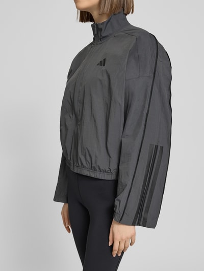 Modelka nosi Regular Fit Jacke mit Stehkragen od adidas Sportswear, ciemnoszary, logo, zamek, elastyczne wykończenia, szerokość w rozmiarze S: 64 cm, długość pleców: 54 cm, rękaw: 48 cm, widok z boku, z przodu