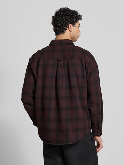 Męski model nosi Regular Fit Freizeithemd mit Logo-Patch Modell 'Edmands' od Carhartt Work In Progress, koszula bawełniana w bordowo-czarną kratę, długi rękaw, kieszenie na piersi, button-down kołnierzyk, sportowe mankiety, widoczne logo; krój regular fit, długość tyłu w rozmiarze M: 76 cm, szerokość w rozmiarze M: 50 cm, długość rękawa w rozmiarze M: 61 cm, widok całej sylwetki z tyłu.