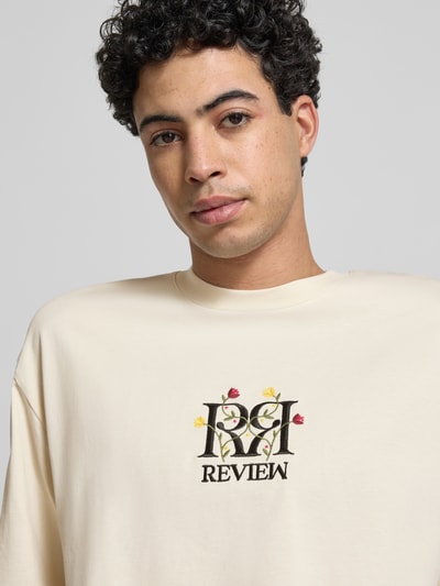 Männermodel trägt Oversized Fit T-Shirt mit Logo-Stitching von REVIEW in Creme, florales Stitching, reine Baumwolle, Nahaufnahme Oberkörper.