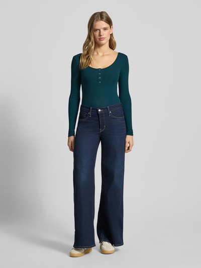 Kobiece model prezentuje Slim Fit Langarmshirt aus Baumwoll-Mix Modell 'KITTE' od Pieces, zielony, prążkowany, dekolt Henley, długi rękaw, widok całej sylwetki z przodu.
