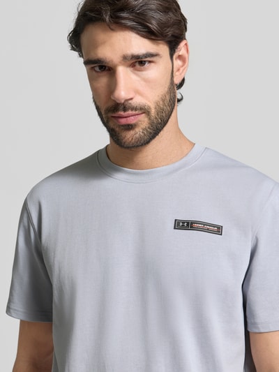Męski model nosi Regular Fit T-Shirt mit Logo-Applikation od Under Armour, bawełniana mieszanka, okrągły dekolt, krój regular fit, długość pleców w rozmiarze M: 73 cm, jasnoszary, gładka struktura, detal logo, zbliżenie na górną część ciała