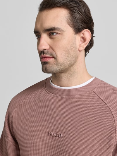 Männermodel trägt Regular Fit Sweatshirt aus reiner Baumwolle Modell 'DAFFLYN' von HUGO in Altrosa, Jacquardstruktur, Nahaufnahme Oberkörper.