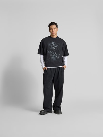 Männermodel trägt Relaxed Fit T-Shirt aus Baumwolle von VETEMENTS, Schwarz mit Motiv-Print, Destroyed-Look, Ganzkörperansicht von vorne.