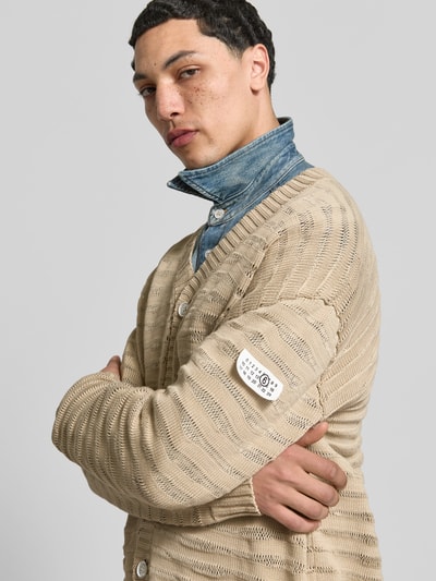 Männermodel trägt Relaxed Fit Cardigan in Strick-Optik von MM6 Maison Margiela aus Reiner Baumwolle in Beige mit V-Ausschnitt und Knopfleiste, Nahaufnahme Oberkörper. Rückenlänge bei Größe M: 76 cm, Schulterbreite: 45 cm, Ärmellänge: 78 cm.