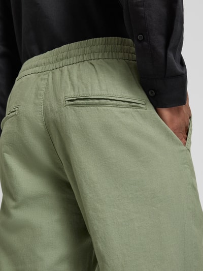 Männermodel trägt Straight Fit Leinenhose mit elastischem Bund Modell 'Barton' von Matinique, mieszanka lnu i bawełny, model męski, szerokość w rozmiarze M: 34 cm, długość wewnętrzna nogawki: 78 cm, zielony, tekstura gładka, z tyłu kieszenie, detailaufnahme Rückansicht.