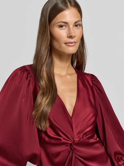 Frauenmodel trägt Cocktailkleid mit Knotendetail und V-Ausschnitt Modell 'THEA' von YAS in A-Linie aus glänzendem Stoff, Nahaufnahme Oberkörper.