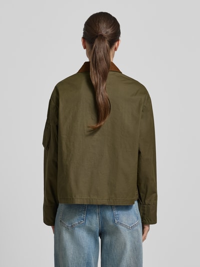 Frauenmodel trägt Jacke aus Baumwolle mit Pattentaschen von Original Bombers in Olivgrün, Regular-Fit, Rückenansicht, Ganzkörperansicht Rückansicht. Das Material ist Reine Baumwolle, Umlegekragen, Knopfleiste, Rückenlänge bei Größe S: 60 cm, Schulterbreite: 52 cm, Brustweite: 58 cm, Ärmellänge: 57 cm, hervorstechende glatte Struktur und dezenter Glanz.