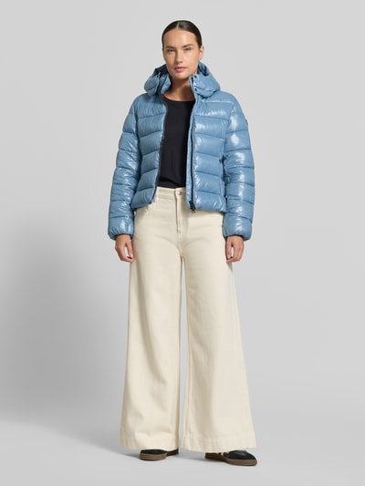 Frauenmodel trägt Jacke in Stepp-Optik Modell 'Mary' von Save The Duck in Hellblau mit Kapuze und Zweiwegereißverschluss, Ganzkörperansicht von vorne. Die Jacke zeigt eine taillierte Passform mit Stehkragen, Eingrifftaschen mit Reißverschluss, dazu cremefarbene weite Hose, der leicht glänzende Stoff hebt die strukturierte Oberfläche hervor, Kontext: Damen Jacke, Rückenlänge 53 cm, Schulterbreite 44 cm, Brustweite 41 cm, Ärmellänge 66 cm.