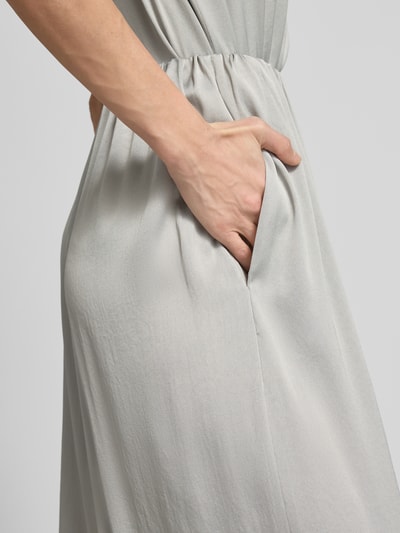 Kobiece model prezentuje spodnie materiałowe Loose Fit Stoffhose mit Stretch-Anteil od Drykorn, mieszanka acetatu i elastanu, krój loose fit, elastyczny pas, szerokie nogawki, szerokość w rozmiarze 27/34: 35 cm, długość wewnętrzna nogawki: 76 cm, jasnoszary kolor, gładka tekstura, detal kieszeni. Zbliżenie na bok biodra.