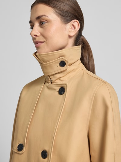 Frauenmodel trägt Trenchcoat mit Ärmelriegeln von Stefanel in Beige mit schwarzen Knöpfen, reine Baumwolle, Nahaufnahme Oberkörper.