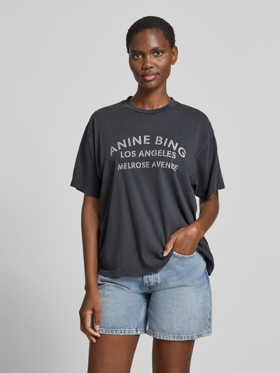 Frauenmodel trägt Relaxed Fit T-Shirt mit Logo-Print von Anine Bing aus reiner Baumwolle, Rundhalsausschnitt, kurzärmelig, dunkel und glatt, Rückenlänge bei Größe S 59 cm, Ganzkörperansicht von vorne.