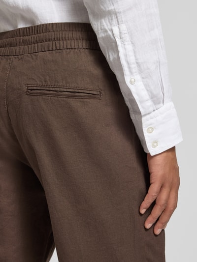 Mannenmodel draagt Straight Fit Leinenhose mit elastischem Bund Modell 'Barton' van Matinique, linnenmix, bruine kleur, detailopname heup, context: rechte fit, elastische tailleband met tunnelkoord, achterzakken, taillewijdte maat M 34 cm, binnenbeenlengte maat M 78 cm.
