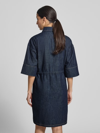 Frauenmodel trägt Knielanges Jeanskleid mit Brusttaschen von Comma aus Reine Baumwolle, Gerader-Schnitt, Knielänge, Hemdblusenkragen, Brusttasche, Knopfleiste, Bindegürtel in dunklem Jeansblau, rechteckige Form mit sichtbaren Nähten, glatte Textur, Ganzkörperansicht Rückansicht.