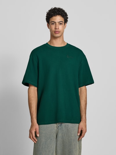 Männermodel trägt Oversized T-Shirt mit Logo-Stitching von KARL KANI in Dunkelgrün, Reine Baumwolle, Oversized-Fit, Rundhalsausschnitt, Herren T-Shirt, Rückenlänge bei Größe M: 73 cm, Ganzkörperansicht von vorne.