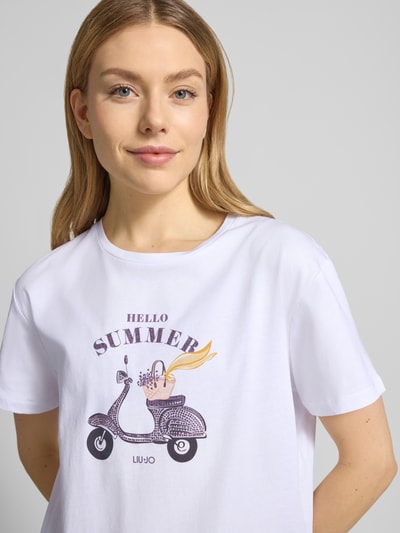 Frauenmodel trägt T-Shirt mit Motiv und Ziersteinbesatz von Liu Jo White in Weiß, reine Baumwolle, Rundhalsausschnitt, Nahaufnahme Oberkörper.