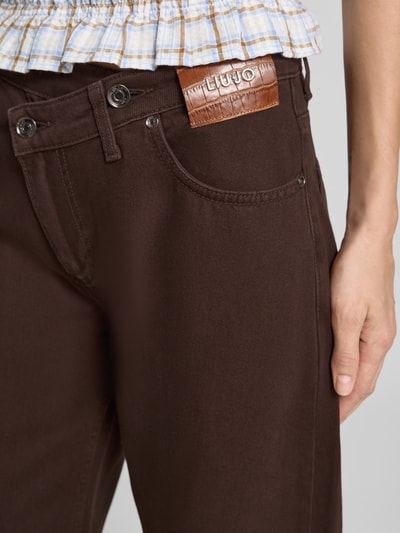Frauenmodel trägt Wide Fit Jeans aus reiner Baumwolle in asymmetrischem Look von Liu Jo White, brauner Stoff, 5-Pocket-Design, Nahaufnahme Oberkörper.