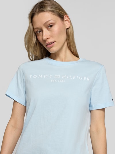 Frauenmodel trägt Regular Fit T-Shirt aus reiner Baumwolle von Tommy Hilfiger in Optik: Unifarben, Logo-Detail, Label-Schriftzug, Rundhals, Kurzarm, Materialverarbeitung: Jersey, Nahaufnahme Oberkörper.