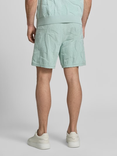 Männermodel trägt Regular Fit Sweatshorts aus Baumwoll-Mix Modell 'ASURFER' von BOSS Orange in Optik: Unifarben mit Struktur, Label-Patch, elastischem Bundabschluss mit Tunnelzug, Eingrifftaschen, Materialverarbeitung: Frottee, Farbe Hellblau, Ganzkörperansicht Rückansicht.