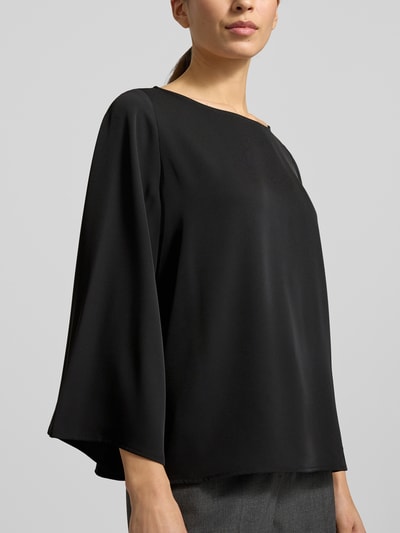 Modelka nosi Blusenshirt mit Rundhalsausschnitt von comma, czarny materiał z domieszką stretchu, luźny krój, widok na górną część ciała z przodu. Długość tyłu w rozmiarze 36: 59 cm, długość rękawa w rozmiarze 36: 52 cm.