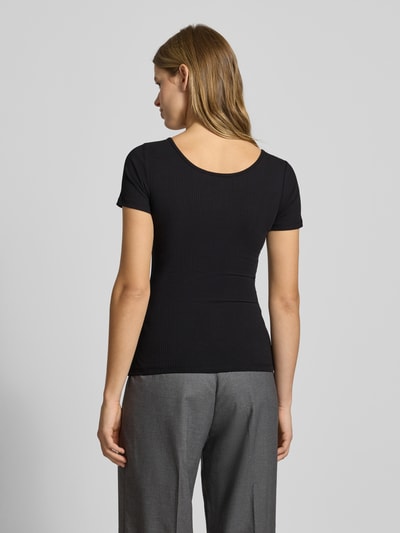 Frauenmodel trägt T-Shirt mit kurzer Druckknopfleiste Modell 'KITTE' von PIECES, schwarze Ripp-Optik, Baumwoll-Elasthan-Mix, Gerader Schnitt, Ganzkörperansicht Rückansicht.