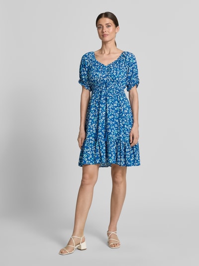 Frauenmodel trägt Minikleid aus Viskose mit Kordelzug und Quasten von Apricot in Blau mit floralen Mustern, taillierter Schnitt, Rundhalsausschnitt mit Rüschen, Rüschenärmel, Smok-Details, Rückenlänge bei Größe S 82 cm, Brustweite 34 cm, Ärmellänge 21 cm, Ganzkörperansicht von vorne.