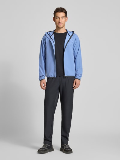 Mannelijk model draagt Regular Fit functioneel jack uit waterdicht materiaal model 'L_COMMUTER' van BOSS Green, look: effen, pasvorm: regular fit, kraagmodel: capuchon, sluiting: ritssluiting, applicatie: reflecterende details, labelprint, mouwvorm: lange mouw, mouwboord: paspelnaad, elastisch, rompzoom: paspelnaad, elastisch, functie: waterdicht, warmte-isolatie, zakken: zij-ritszak, effen lichtblauw met zwarte details, gladde textuur, recht model, geheel zichtbare voorkant, full body vooraanzicht.