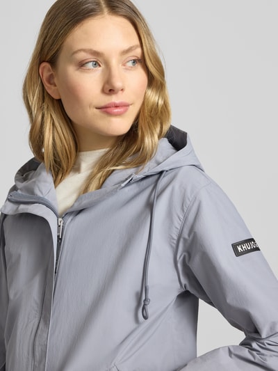 Frauenmodel trägt khujo Parka mit Label-Patches Modell 'AMETI' in Hellgrau, Kapuze mit Kordelzug, verdeckter Reißverschluss, Nahaufnahme Oberkörper. Kontext: Damen Parka, Gerader-Schnitt, Seitliche Pattentaschen, elastische Ärmelabschlüsse, Rückenlänge bei Größe S 81 cm, Schulterbreite 46 cm, Brustweite 50 cm, Ärmellänge 55 cm.