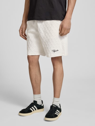 Mężczyznamodel nosi Shorts mit Logo-Stitching Modell 'Jovren' od Pegador, biały materiał, wzór w romby, krój loose fit, elastyczny pas, kieszenie francuskie, szerokość w rozmiarze M 38 cm, długość wewnętrzna nogawki 24 cm, widok całej sylwetki z przodu.