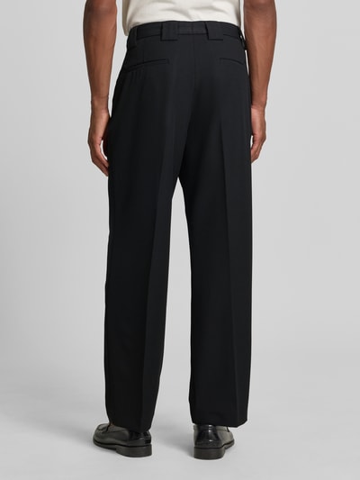 Męski model nosi Stoffhose mit Bügelfalten und Eingrifftaschen od MCNEAL, czarny materiał, krój loose fit, widok całej sylwetki z tyłu. Szerokość w rozmiarze 50: 34 cm, długość nogawki wewnętrznej: 80 cm, mieszanka materiałów z dodatkiem wiskozy, francuskie kieszenie, tylne kieszenie z lamówką.