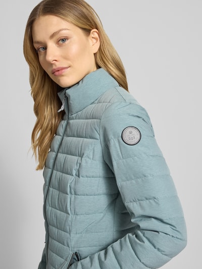 Kobiece modelka nosi kurtkę pikowaną z zamkiem błyskawicznym i kieszeniami zapinanymi na zamek błyskawiczny G.I.G.A. DX Steppjacke mit Reißverschlusstaschen Modell 'GS 111', krój slim fit, stójka, długość tyłu w rozmiarze 36: 67 cm, szerokość ramion w rozmiarze 36: 38 cm, szerokość klatki piersiowej w rozmiarze 36: 49 cm, długość rękawów w rozmiarze 36: 65 cm, jasnoniebieski, detaliczna faktura tkaniny, widok z przodu – zbliżenie na górną część ciała.