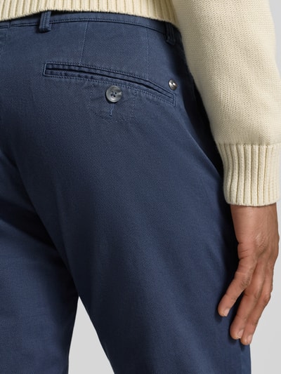 Męski model nosi Fein strukturierte Chino mit Gesäßtaschen od Bugatti, mieszanka bawełny z dodatkiem streczu, krój regular fit, wpuszczane i tylne kieszenie, kolor granatowy, delikatna faktura, szerokość w rozmiarze 32/32: 40 cm, długość wewnętrzna nogawki: 82 cm, detaliczne ujęcie tylnej części.