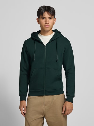Männermodel trägt Regular Fit Sweatjacke aus Baumwoll-Mix Modell 'BRADLEY' von JACK & JONES in Dunkelgrün mit Kapuze und Känguru-Tasche, Ganzkörperansicht von vorne, Herren Sweatjacke, elastische Abschlüsse, separater Tunnelzug, Rückenlänge 67 cm, Ärmellänge 68 cm.