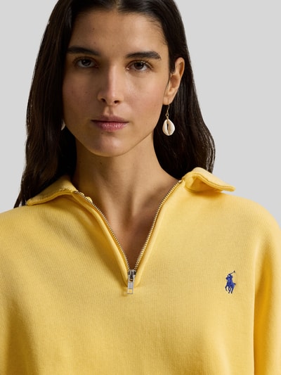 Vrouwenmodel draagt 'Sweatshirt mit Label-Stitching' van Polo Ralph Lauren in geel, katoenmengsel, losse snit, polokraag, korte rits, label-stitching en geribde boorden. Close-up bovenlichaam.