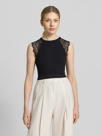 Kobiece modelka nosi Crop Top mit Spitzenbesatz Modell 'MILLIE' von Guess, czarny, materiał z domieszką stretchu, krój slim fit, cropped, koronkowe detale, długość tyłu 37 cm w rozmiarze S, widok całej sylwetki z przodu.