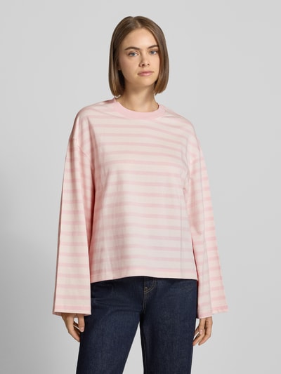 Modelka nosi Relaxed Fit Langarmshirt aus reiner Baumwolle od Gina Tricot, bawełna, krój relaxed fit, okrągły dekolt, długi rękaw, długość tyłu 62 cm w rozmiarze S, różowe paski, matowa tekstura, pełny widok z przodu.
